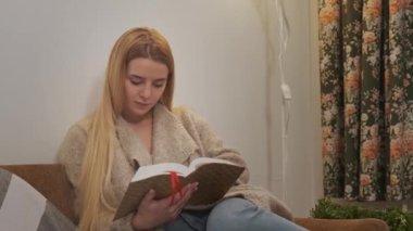 Genç bir kadın sandalyesinde rahatlıyor ve kitabı karıştırıyor..