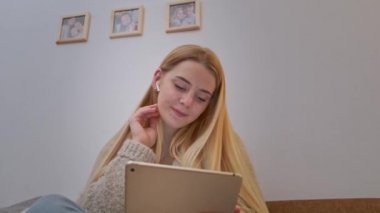 Kanepede oturan, internette sörf yapan ve dijital tablette dans eden genç bir kadın..