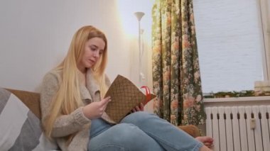 Genç bir kadın sandalyesinde rahatlıyor ve kitabı karıştırıyor..