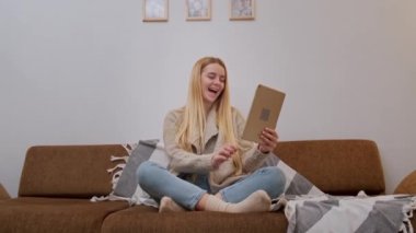 Mutlu gülümseyen genç kadın kanepede oturuyor, arkadaşı tablet kullanarak arıyor.