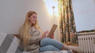 Mutlu gülümseyen genç kadın kanepede oturuyor, arkadaşı tablet kullanarak arıyor.