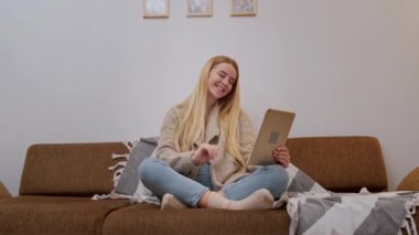 Mutlu gülümseyen genç kadın kanepede oturuyor, arkadaşı tablet kullanarak arıyor.