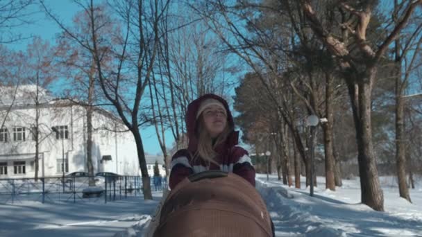 Una joven madre camina con su hijo en un cochecito en un día claro de invierno. — Vídeos de Stock