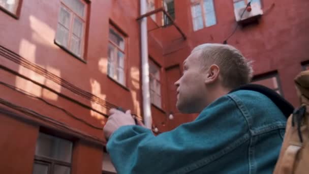 Un joven viajero toma fotos de un edificio de ladrillo rojo en un casco antiguo — Vídeo de stock