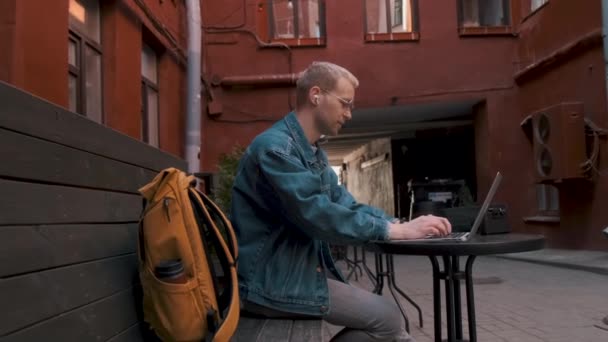 Podróżnik pracuje na laptopie siedząc przy stoliku w kawiarni. — Wideo stockowe