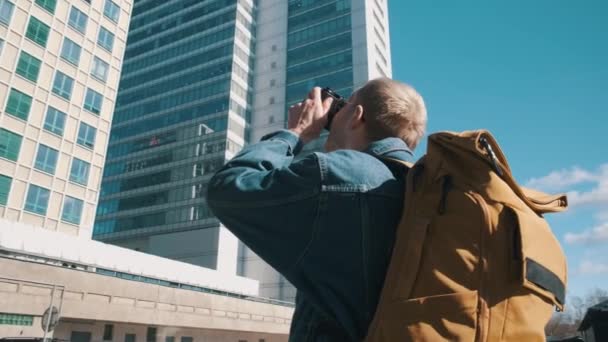 Un viaggiatore di sesso maschile con uno zaino giallo scatta foto della città sulla macchina fotografica. — Video Stock