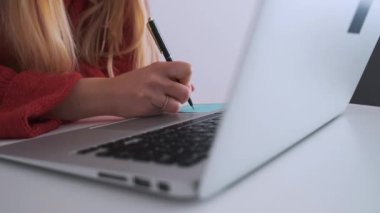 Laptopta çalışırken not alan genç bir kız öğrenci. Çevrimiçi çalışma.