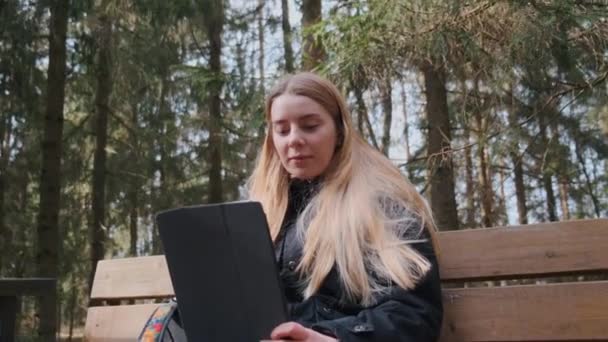 En vacker ung blond kvinna som har en videokall när du reser i skogen — Stockvideo