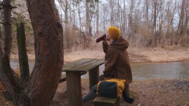 Joven viajero sentado a la orilla del río bebiendo té y admirando relajante — Vídeos de Stock