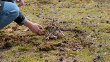 Genç erkek, çubuklarla küçük bir orman kamp ateşi yakıyor ve ellerini ısıtıyor..