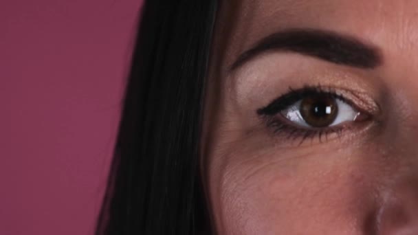 Detailní záběr na hnědé oko krásné brunetky žena usmívá na růžovém pozadí. — Stock video
