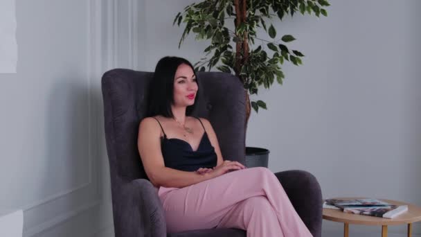 Exitosa hermosa mujer de negocios morena da una entrevista sentado en el sillón marrón. — Vídeos de Stock