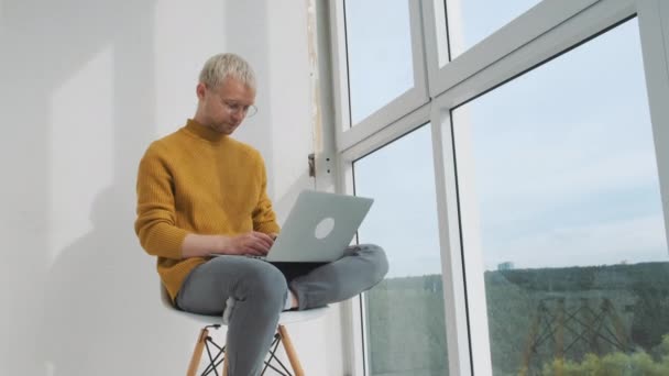 Retrato de um jovem freelancer europeu sentado na varanda com o laptop multitarefa. — Vídeo de Stock