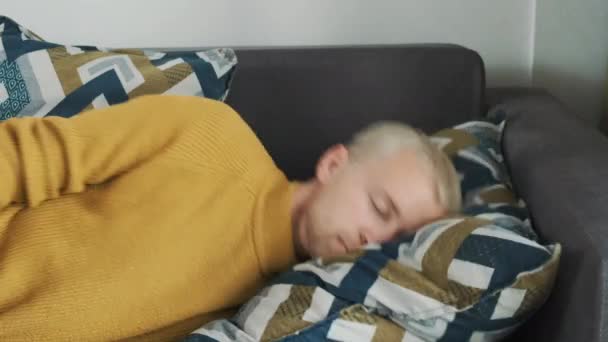 Junge europäische erschöpfte oder gelangweilte Männchen fällt nach einem anstrengenden Arbeitstag buchstäblich auf das Sofakissen und schläft ein. — Stockvideo