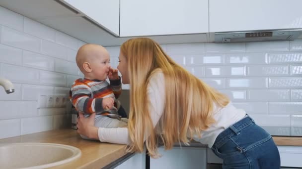 Młoda atrakcyjna blondynka matka bawi się i śmieje ze swoim synkiem siedzącym na kuchennym stole. — Wideo stockowe