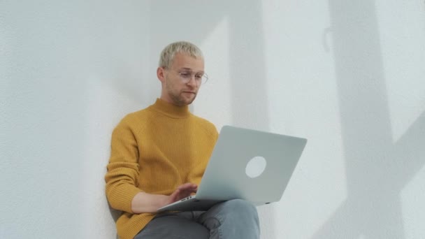 Retrato de un joven freelancer europeo sentado en el balcón con el portátil multitarea. — Vídeos de Stock