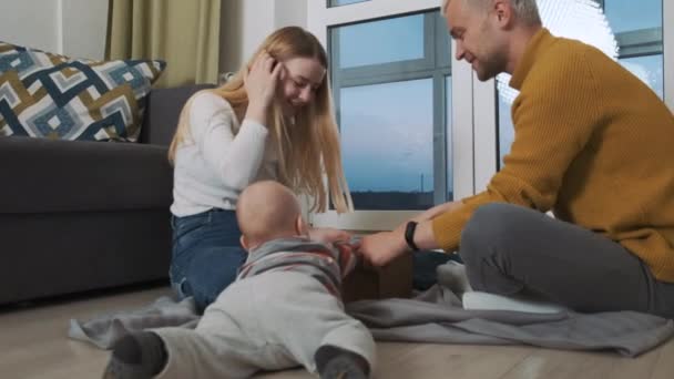 A fiatal és boldog háromtagú európai család kinyitja a jelenlegi doboz poharát. Élvezik a meglepetést és beszélgetnek az érzéseikről.. — Stock videók