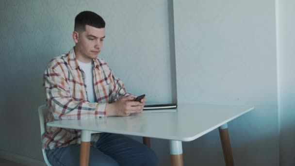 Młody europejski freelancer pracuje w domu, przy stole przy użyciu smartfona, pijąc filiżankę herbaty. — Wideo stockowe