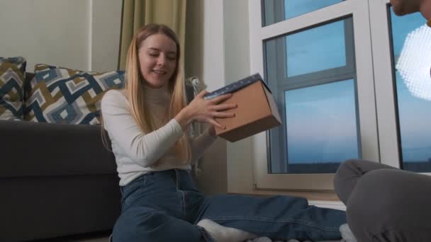 Young and happy european couple is opening the cup of the present box. Enjoying the surprise and having a conversation about their feelings. — Stock Video