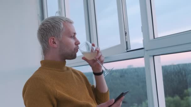 Slow motion shot af een jonge Europeaan drinken wijn op het balkon genieten van het uitzicht en de zonsondergang. — Stockvideo