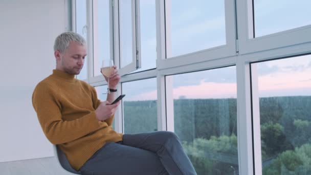 バルコニーで景色を楽しみながら夕日を眺めながらワインを飲む若いヨーロッパの男. — ストック動画
