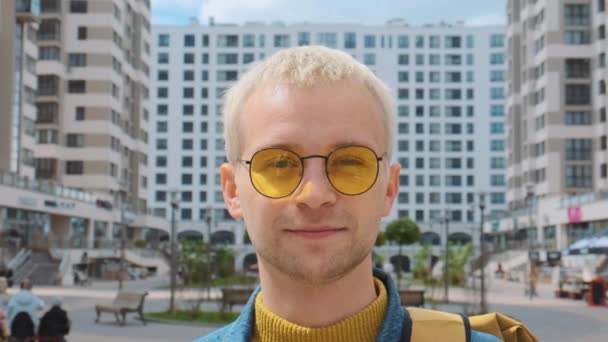 Retrato de un joven atractivo rubio europeo sonriente con gafas amarillas mirando a la cámara. — Vídeos de Stock