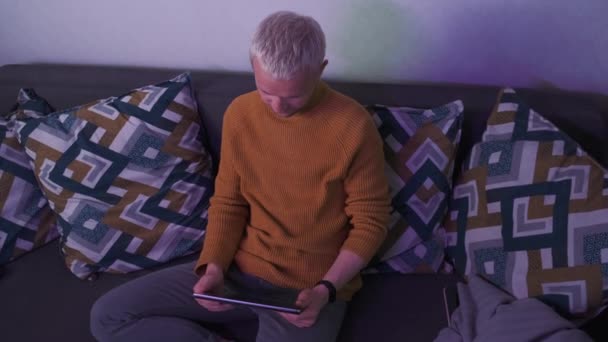 Top shot de un hombre europeo sosteniendo la tableta mientras está sentado en el sofá por la noche. Freelancer o jugador de juego. — Vídeos de Stock
