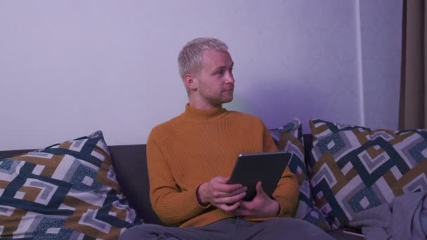 Top-Aufnahme eines europäischen Männchens, das die Tablette hält, während es abends auf dem Sofa sitzt. Freiberufler oder Spieler. — Stockvideo