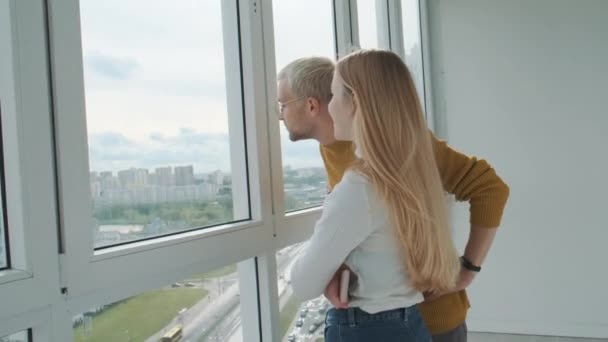 Joven pareja europea tiene una conversación de pie en un gran balcón de luz con ventanas panorámicas. — Vídeos de Stock