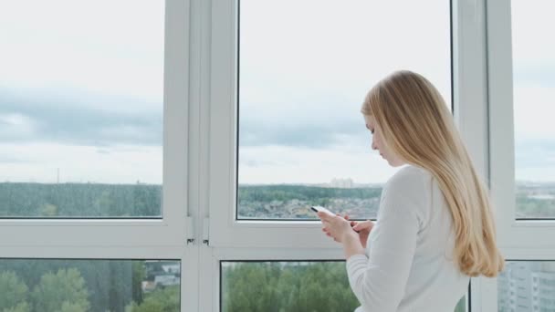 Junge energische Geschäftsfrau telefoniert mit einem Kunden vor einem riesigen Panoramafenster mit Blick auf die Stadt. — Stockvideo