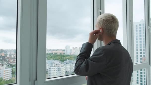 Young energetic businessman talking to a client by phone in front of a huge panoramic window with the city view. — Stock Video