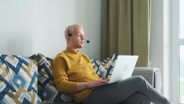 Jonge mannelijke Europese freelancer werkt online, praten met de klant bespreken van nieuwe projecten zitten op de bank thuis. — Stockvideo