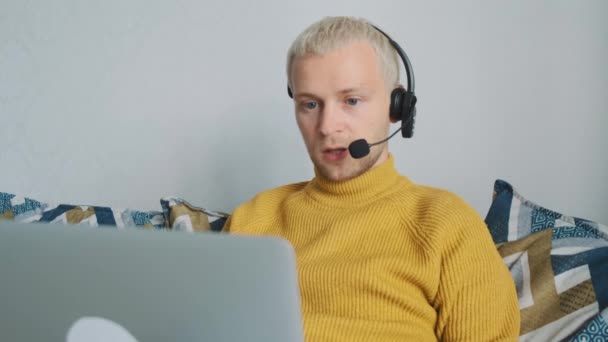Çevrimiçi çalışan Avrupalı genç bir erkek, müşteriyle konuşuyor ve evdeki kanepede oturan yeni projeleri tartışıyor.. — Stok video