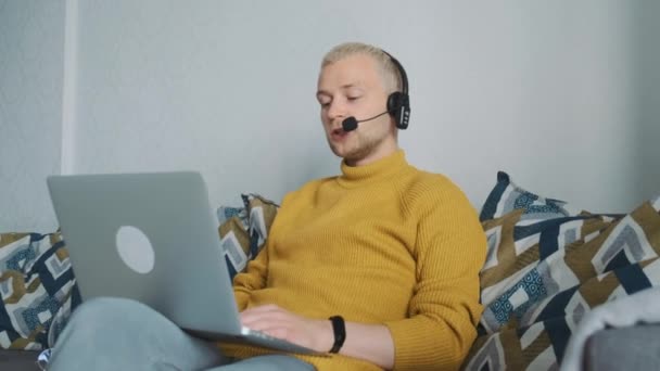 若い男性ヨーロッパのフリーランスがオンラインで仕事をし、自宅でソファに座っている新しいプロジェクトを議論するクライアントと話をします。. — ストック動画