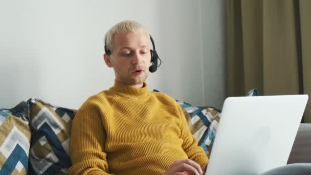 Fiatal férfi európai szabadúszó online dolgozik, beszél az ügyfél megvitatása új projektek ül a kanapén otthon. — Stock videók