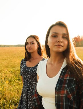İki kız kardeş doğada yürüyor ve iletişim kuruyor. Gün batımında fotoğraf çekiyorlar..