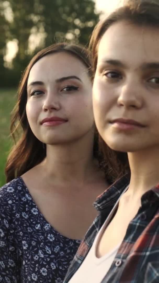 Dos hermanas jóvenes miran misteriosamente a la lente de la cámara. Vídeo vertical. — Vídeo de stock