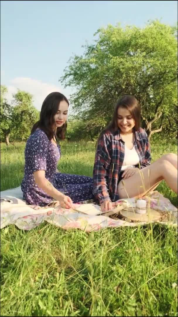 Dos hermanas caminan en la naturaleza, se comunican, comparten secretos y leen un libro. Vídeo vertical. — Vídeo de stock