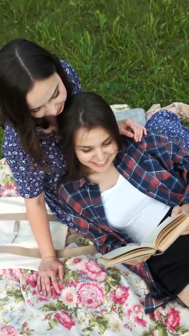 Dwie siostry chodzą w naturze, komunikują się, dzielą sekretami i czytają książkę. Pionowe wideo. — Wideo stockowe