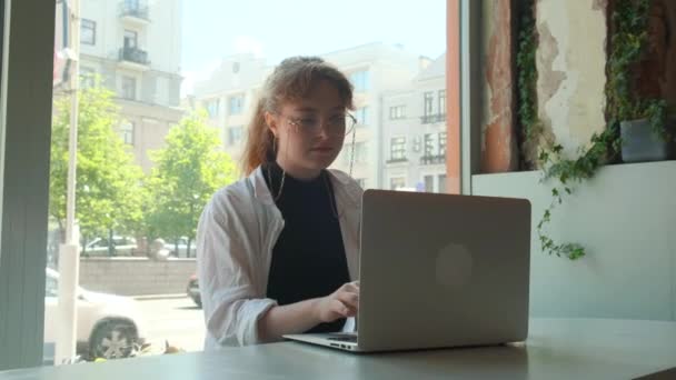 Uma jovem trabalha remotamente em um café em um terraço de verão. Um freelancer trabalha ao ar livre. — Vídeo de Stock