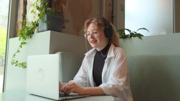 Een jong meisje werkt op afstand in een café op een zomerterras. Een freelancer communiceert met collega 's via videolink. — Stockvideo