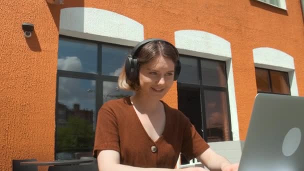 Una giovane ragazza lavora a distanza in un caffè su una terrazza estiva. Un freelance comunica con i colleghi tramite collegamento video. — Video Stock