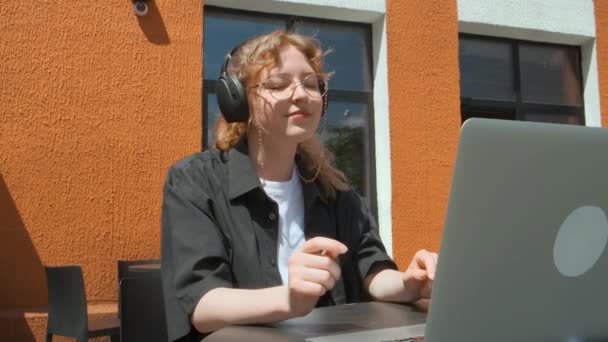 En ung flicka arbetar på distans i ett café på en sommarterrass. En frilansare kommunicerar med kollegor via videolänk. — Stockvideo