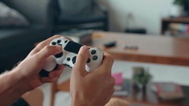 Geniş ekran bir televizyonun önündeki oyun konsolunda video oyunu oynayan bir gencin ellerini yakın plan çekiyoruz.