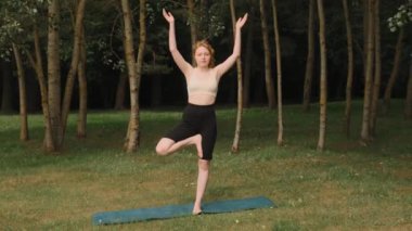 Genç bir kız halka açık bir parkta temiz havada yoga yapıyor..