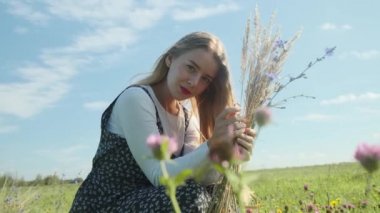 Güzel elbiseli genç bir kız dikenli kazık ve buğdayla bir tarlada yürüyor..