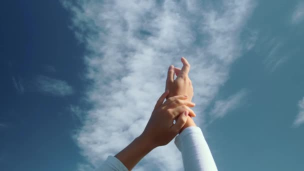 Die Hände eines jungen Mädchens tummeln sich vor dem Hintergrund eines blauen Himmels mit Wolken. — Stockvideo