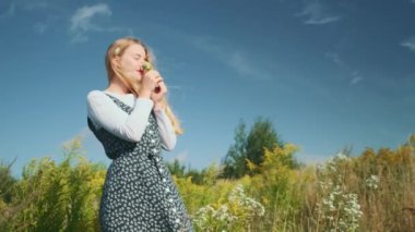 Güzel elbiseli genç bir kız kır çiçeklerini kokluyor. Gökyüzüne karşı güzel manzara.