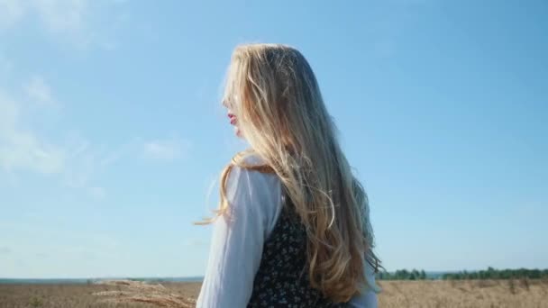 Una joven con un hermoso vestido camina por un campo con espiguillas y trigo. — Vídeos de Stock