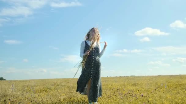 Młoda dziewczyna cieszy się wolnością. Dziewczyna tańczy na polu zupełnie sama z bukietem dzikich kwiatów. — Wideo stockowe